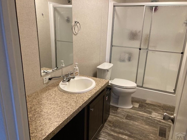 full bathroom featuring toilet, wood finished floors, visible vents, vanity, and a shower stall