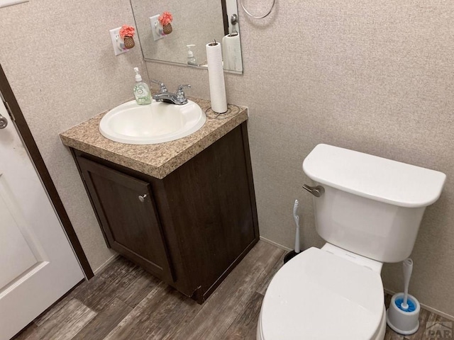 bathroom with toilet, wood finished floors, vanity, and baseboards