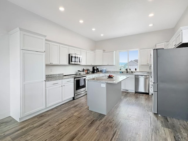 kitchen with white cabinets, light stone counters, stainless steel appliances, wood finished floors, and a center island