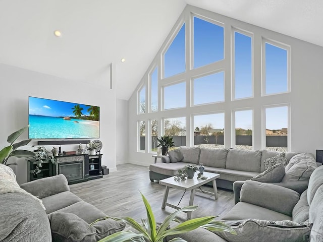 living room with high vaulted ceiling, baseboards, and light wood-style flooring