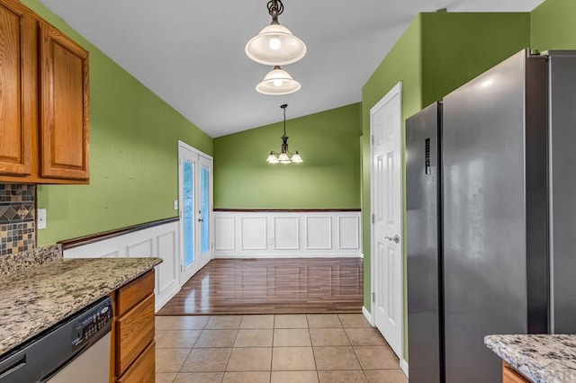 kitchen featuring pendant lighting, light tile patterned floors, brown cabinetry, light stone counters, and stainless steel appliances