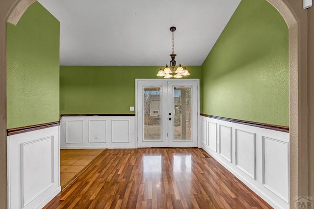 interior space with arched walkways, an inviting chandelier, wood finished floors, french doors, and lofted ceiling