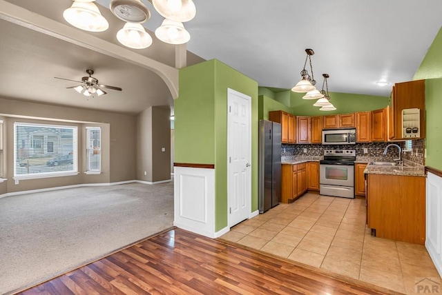 kitchen with a sink, ceiling fan, appliances with stainless steel finishes, brown cabinets, and vaulted ceiling