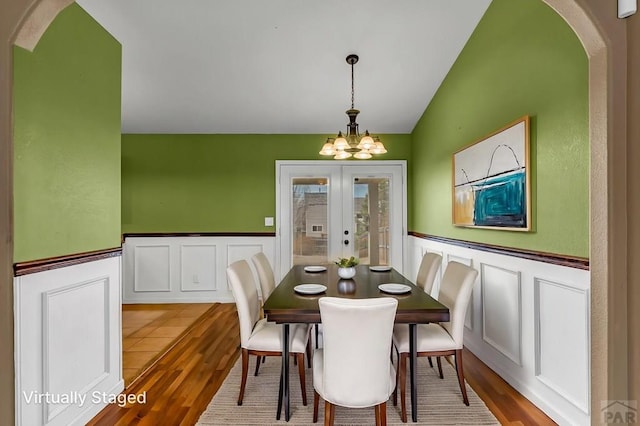 dining space with a chandelier, french doors, a decorative wall, arched walkways, and wood finished floors
