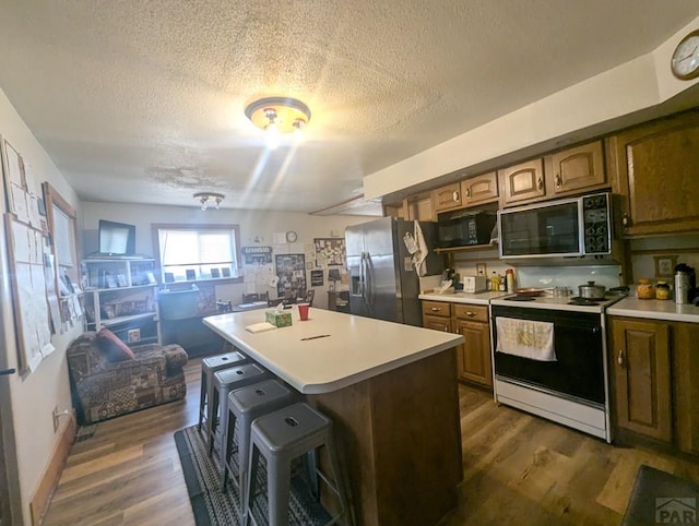 kitchen featuring black microwave, electric range, stainless steel refrigerator with ice dispenser, and a kitchen bar