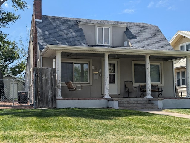 view of front of property with a chimney, a porch, roof with shingles, cooling unit, and a front yard