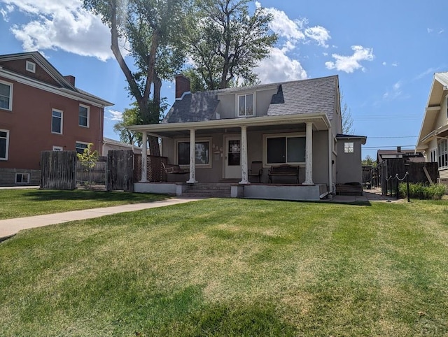 view of front facade featuring fence, a chimney, a porch, and a front lawn