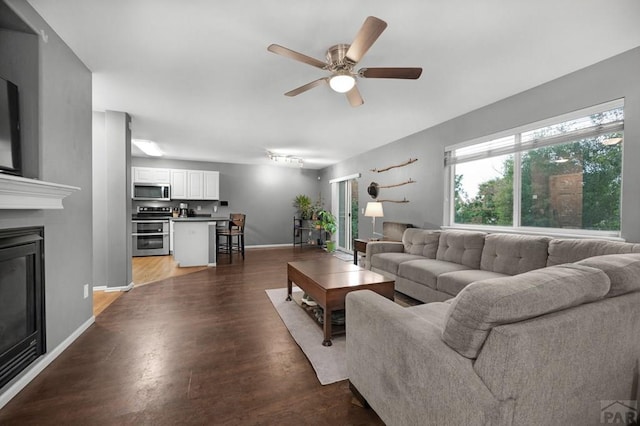7365 Far Hill Dr, Colorado Springs, CO 80922 - living room featuring a glass covered fireplace, a ceiling fan, wood finished floors, and baseboards