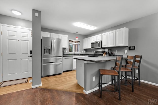 7365 Far Hill Dr, Colorado Springs, CO 80922 - kitchen featuring stainless steel appliances, a peninsula, dark countertops, white cabinetry, and light wood finished floors