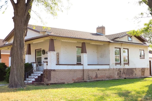 view of front of house with a shingled roof, a front yard, brick siding, and a chimney