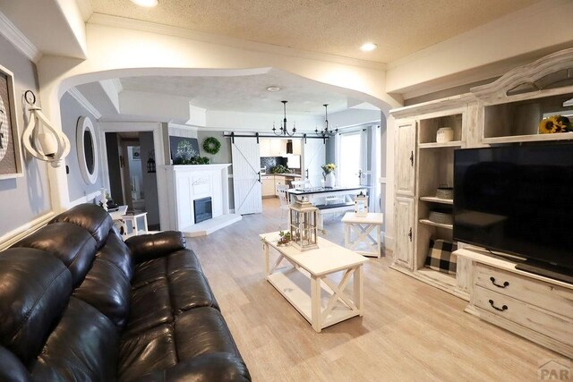 living area featuring a textured ceiling, a barn door, arched walkways, and light wood-style flooring