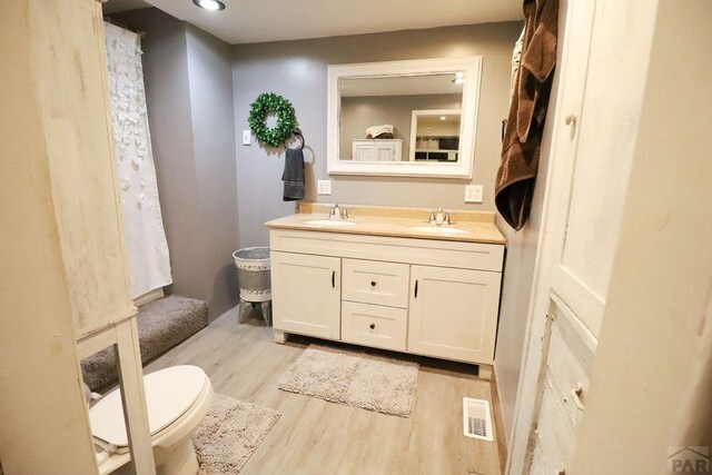 bathroom with double vanity, visible vents, a sink, and wood finished floors