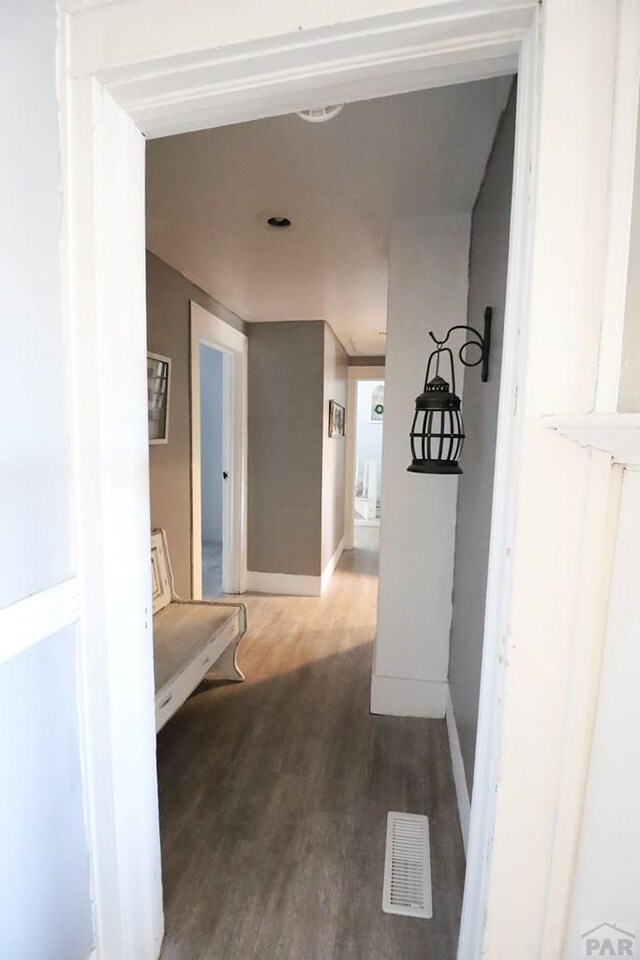 hall featuring dark wood-style flooring, visible vents, and baseboards