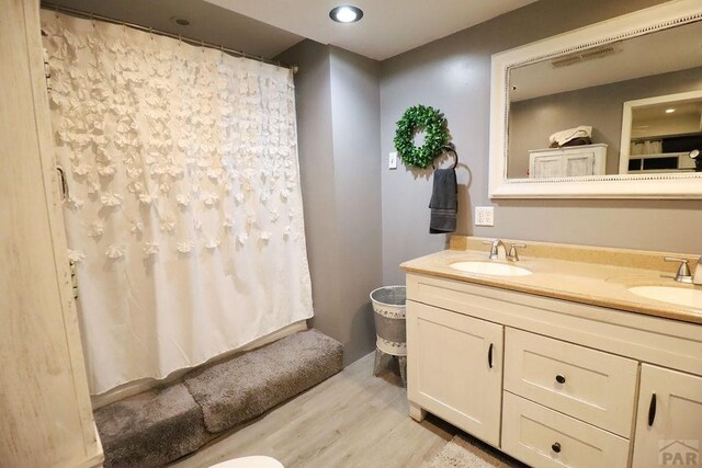 bathroom with double vanity, wood finished floors, a shower with shower curtain, and a sink