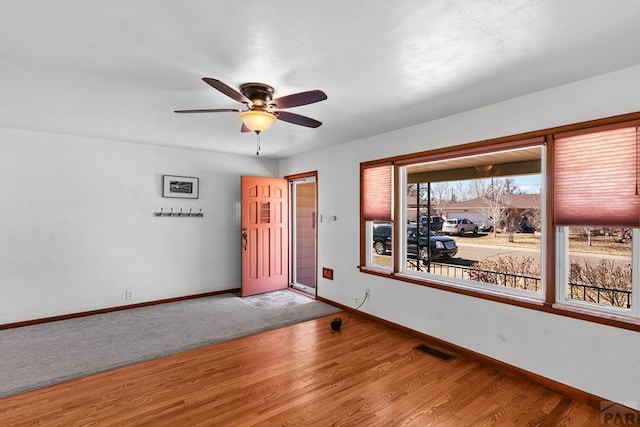 empty room featuring ceiling fan, wood finished floors, visible vents, and baseboards