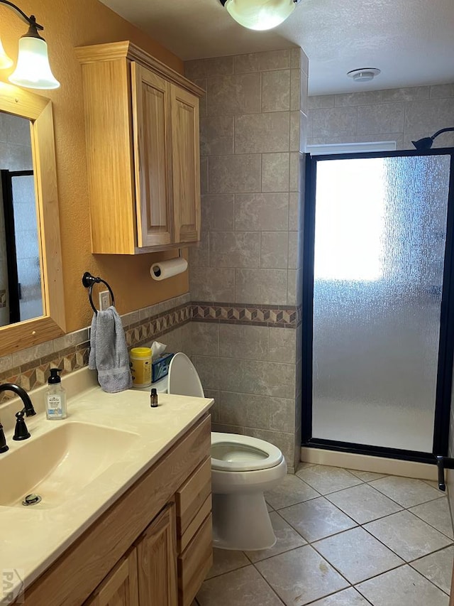 bathroom with tile walls, toilet, a shower stall, vanity, and tile patterned flooring