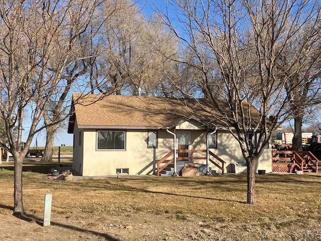 view of front of home with stucco siding, a front yard, and a shingled roof
