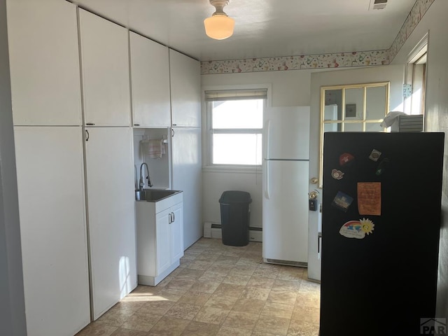 kitchen with white cabinets, a sink, and freestanding refrigerator