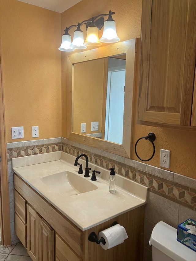 bathroom with toilet, vanity, tile walls, wainscoting, and tile patterned floors