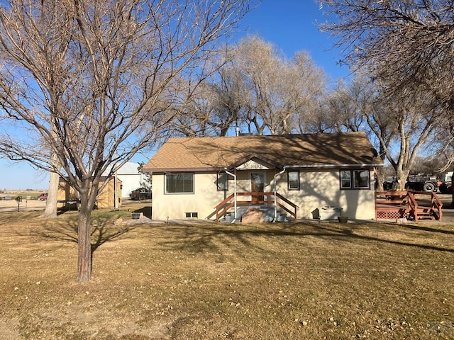 rear view of house featuring stucco siding, a lawn, and roof with shingles