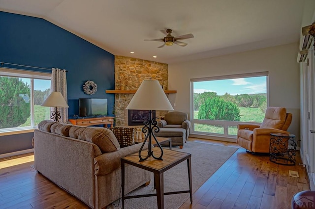 living room with ceiling fan, vaulted ceiling, wood finished floors, and a stone fireplace