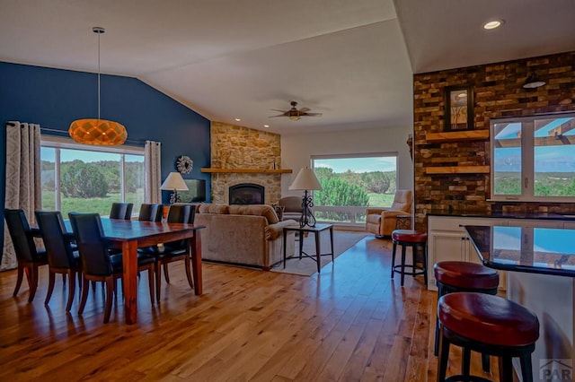 dining space with vaulted ceiling, a fireplace, light wood-style flooring, and a healthy amount of sunlight
