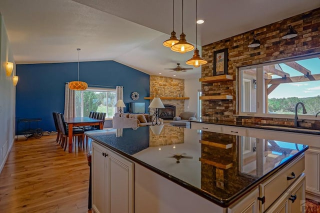 kitchen with dark stone counters, white cabinets, lofted ceiling, decorative light fixtures, and a sink