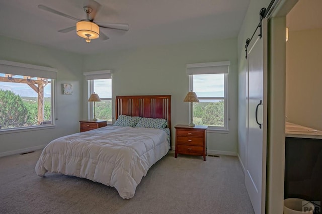 bedroom with baseboards, light carpet, multiple windows, and a barn door