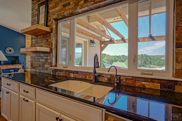kitchen with a sink, white cabinetry, open shelves, and dark stone countertops