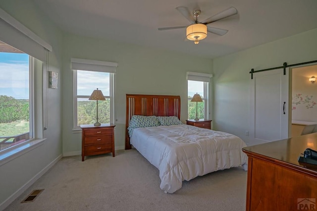 bedroom with ceiling fan, a barn door, light carpet, visible vents, and baseboards