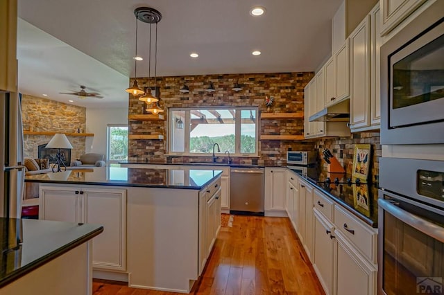 kitchen with stainless steel appliances, dark countertops, open floor plan, and decorative light fixtures