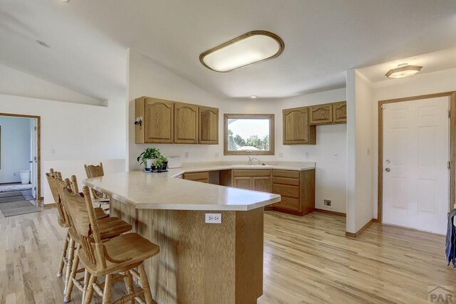 kitchen with a peninsula, light wood-type flooring, a kitchen bar, and light countertops