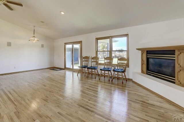 unfurnished dining area featuring lofted ceiling, light wood-style floors, baseboards, and a glass covered fireplace