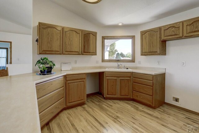 kitchen featuring brown cabinets, vaulted ceiling, light countertops, and a sink