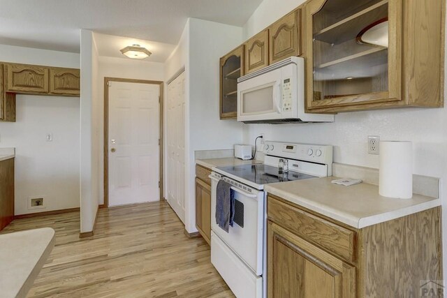 kitchen featuring light countertops, glass insert cabinets, brown cabinetry, light wood-type flooring, and white appliances