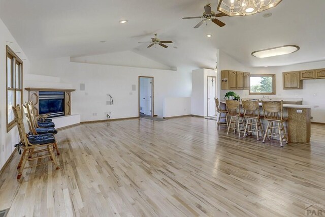 living area with vaulted ceiling, a glass covered fireplace, light wood-style flooring, and baseboards