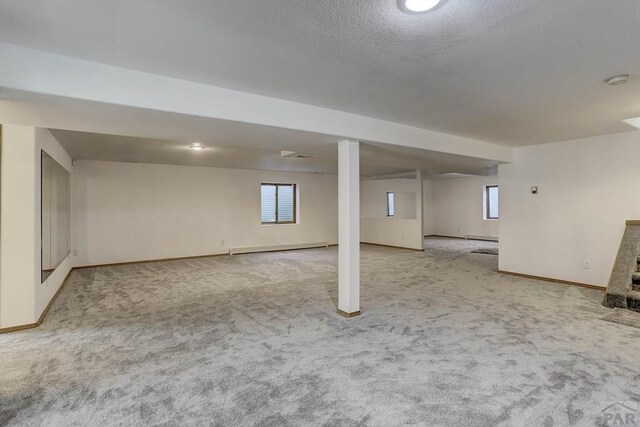 basement with light carpet, a textured ceiling, a baseboard radiator, and baseboards