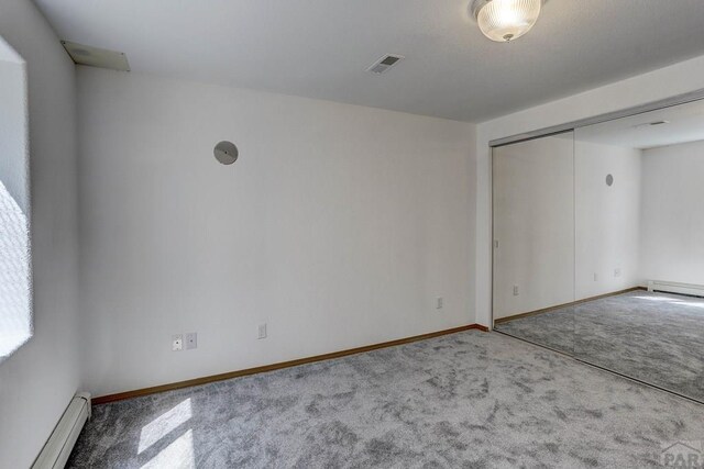 spare room with a baseboard heating unit, carpet, visible vents, and baseboards