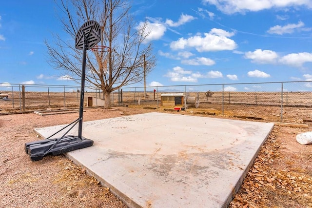 view of basketball court featuring a rural view, fence, and basketball hoop