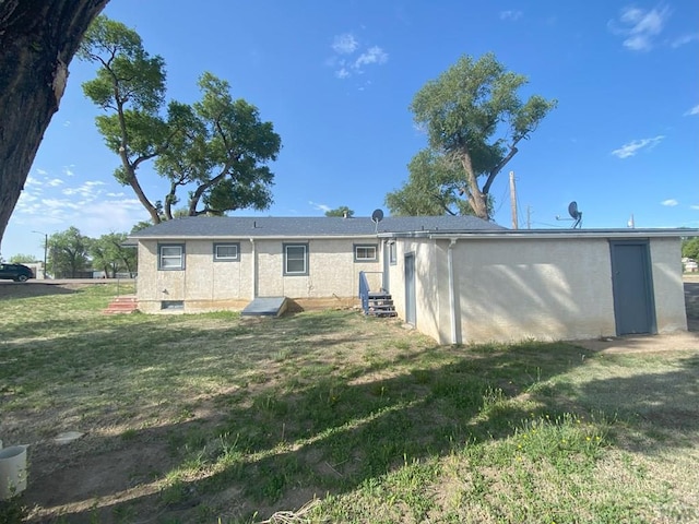 back of property with entry steps, a lawn, and stucco siding
