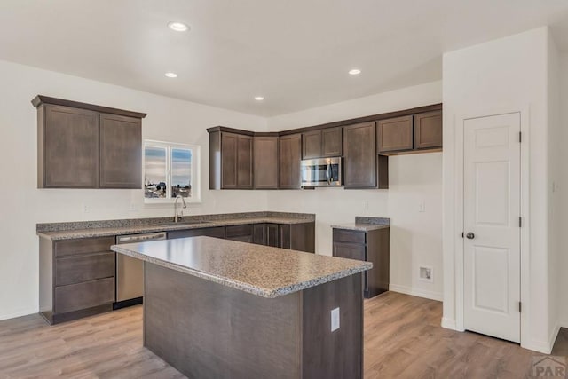 kitchen with appliances with stainless steel finishes, a center island, light wood-type flooring, and a sink