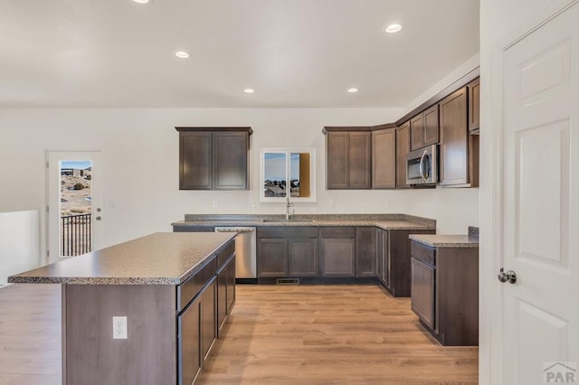 kitchen featuring dark brown cabinetry, light wood finished floors, a kitchen island, stainless steel appliances, and a sink