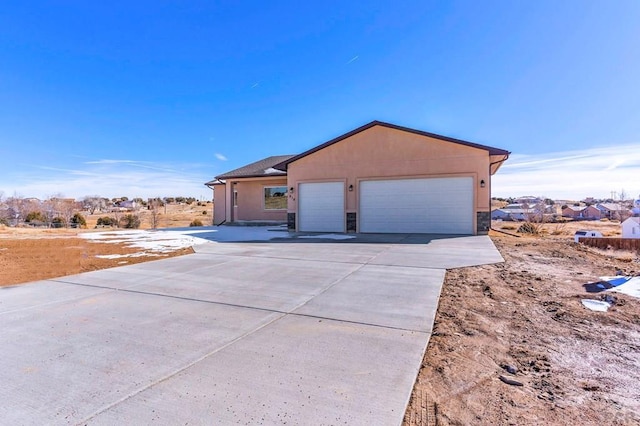 view of side of property with stone siding, concrete driveway, a garage, and stucco siding