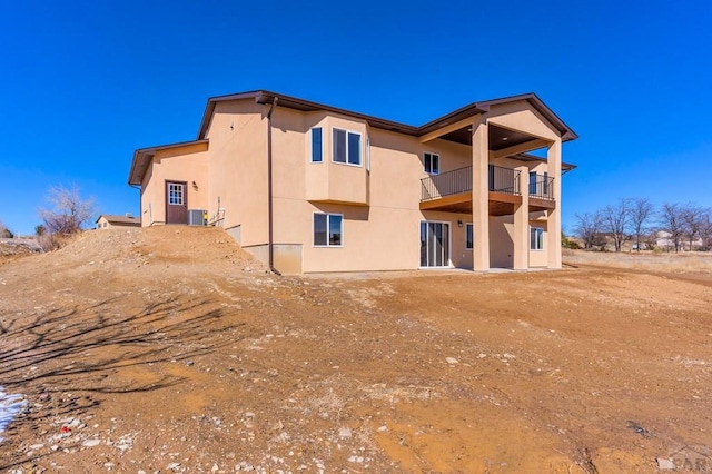 rear view of property with central air condition unit, a balcony, and stucco siding