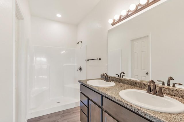 full bathroom featuring wood finished floors, double vanity, a sink, and walk in shower