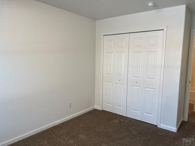 unfurnished bedroom with a closet, dark carpet, and baseboards