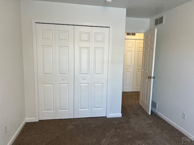 unfurnished bedroom featuring dark colored carpet, a closet, and visible vents