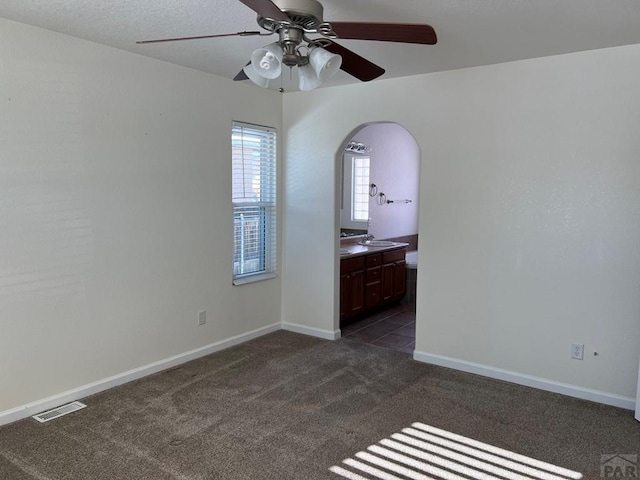 unfurnished bedroom with baseboards, visible vents, dark colored carpet, and connected bathroom