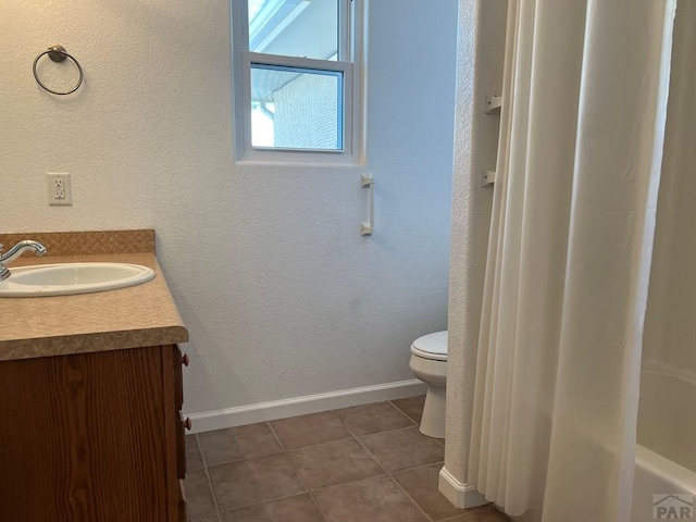 full bathroom featuring a textured wall, toilet, vanity, baseboards, and tile patterned floors