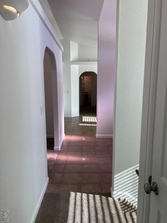 hall featuring arched walkways, a textured wall, dark tile patterned floors, and baseboards